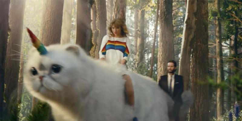 Taylor Swift riding a giant white cat with a rainbow unicorn horn