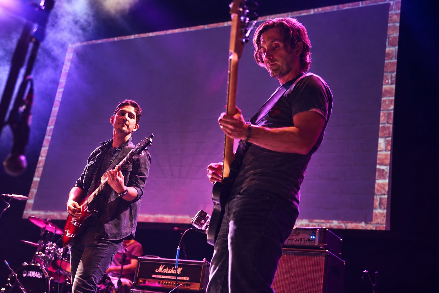 Brandon on bass in the foreground with a coworker on guitar, on stage at AdJam in Los Angeles